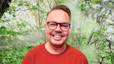Petri Laapas småler in i kameran framför en grönskande bakgrund.