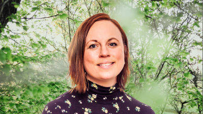Anna Bertills småler in i kameran framför en grönskande bakgrund.