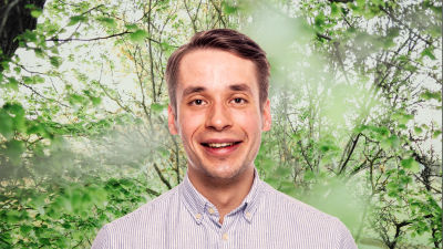 Henrik Wickström ler in i kameran framför en grönskande bakgrund.