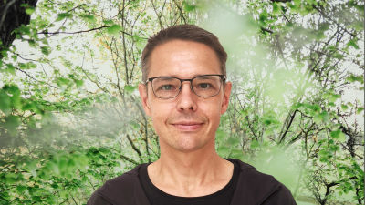 Olof Schybergson småler in i kameran. Bakgrunden är en grönskande skogsdunge.