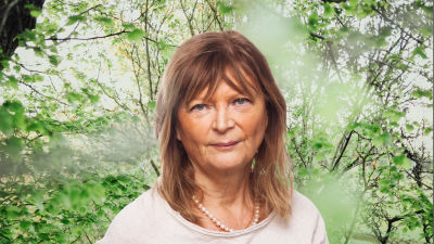 Annika Hällsten ser rakt in i kameran. Bakgrunden är en grönskande skogsdunge.