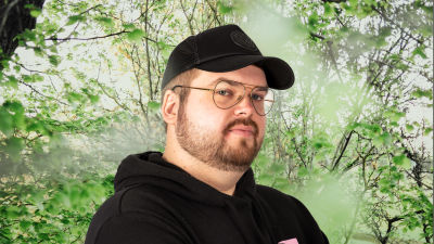 Joel Rönn ser rakt in i kameran. Bakgrunden är en grönskande skogsdunge.