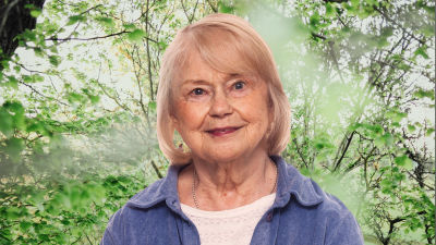Stina Engblom Colliander småler in i kameran framför en grönskande bakgrund.