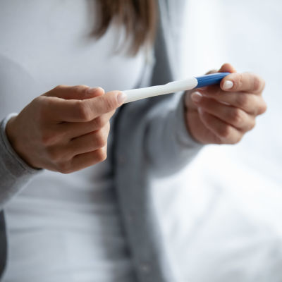 En kvinna håller ett graviditetstest i händerna. Enbart kvinnans händer syns, inte ansiktet.