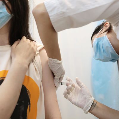 En person sitter ner och håller upp sin skjortärm medan hen får coronavaccin i armen.
