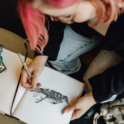 Evelina Blom, en flicka med rödaktigt hår, lutar sig över att ritblock där hon tecknar en fågel.