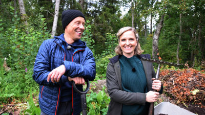 En man och en kvinna som står framför en hög med trädgårdsavfall och hållar i en spade och en kratta.