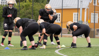 Spelare på gräsplan hukar sig för att ta tag i en amerikansk fotboll.