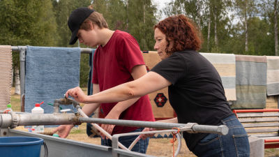 En kvinna och en pojke sträcker sig efter kranen vid en stor balja, de tvättar mattor.