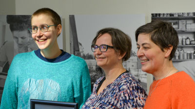Inari Porkka, Outi Norberg och Ulrika Rosendahl står bredvid varandra framför en vägg där det hänger gamla fotografier. 