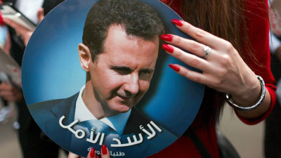 En kvinna som håller i ett porträtt av Syriens president Bashir al-Assad.