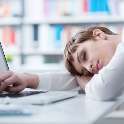 en ung kvinna har somnat vid sin dator.