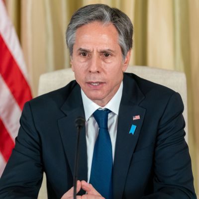 Antony Blinken, USA:s utrikesminister sitter vid ett bord och talar in i en mikrofon i samband med en presskonferens. I bakgrunden syns USA:s flagga.