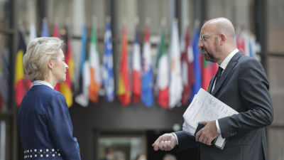 Man och kvinna står vända mot varandra. I bakgrunden europeiska länders flaggor.