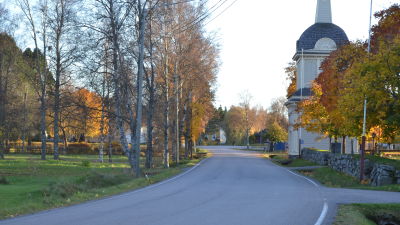 Väg som kurvar sig genom landskap i höstfärger, kyrkobyggnad till höger.