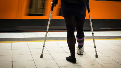 En kvinna med kryckor och foten i paket väntar på perrongen på ett metrotåg.
