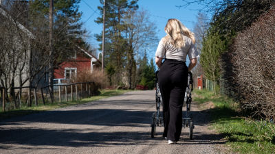 En kvinna promenerar med barnvagn på en grusväg.