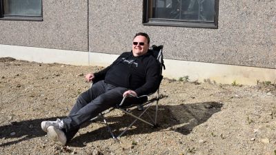 medelålserman sitter i solstol med solglasögon och ler mot kameran