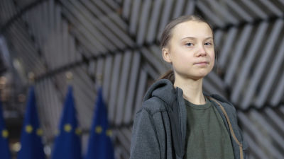 Greta Thunberg står framför Europeiska Unionens flaggor.