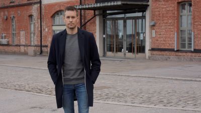 Man i blå jacka utomhus utanför universitetsbyggnad