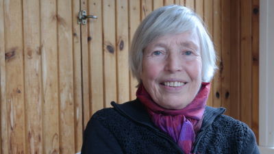 Anita Österberg sitter framför en brun träpanel