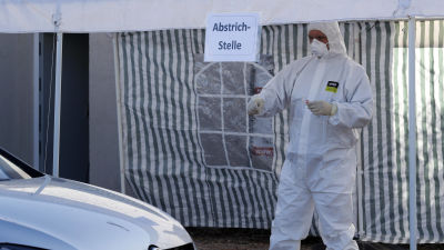 En person i skyddsutrustning går mot en bil för att genomföra ett drive-in coronatest i Landsberg i Tyskland.