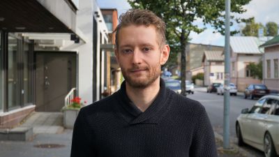 Man i svart tröja står på en trottoar.