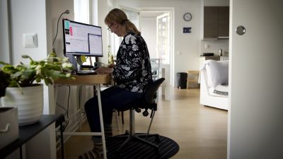 En kvinna sitter inne i sitt hem och jobbar vid en dator.