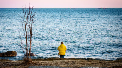En kvinna i gul jacka står vid havet och tittar mot horisonten.