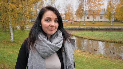 Kvinna i svart jacka står i en park.