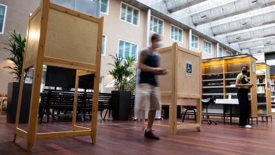 Kaksi äänestyskoppia kirjaston äänestyspisteellä. Mies kävelee ulos äänestyskopista, vaalityöntekijä katsoo sivusta. Miestä ei tunnista kuvasta.