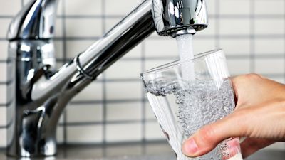 Människa fyller vattenglas under kranen