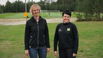 Två kvinnor står vid en sportplan.