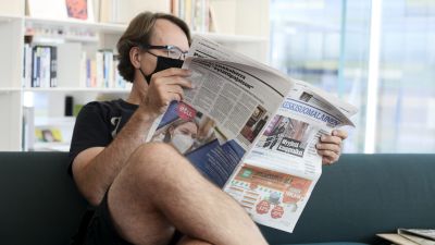 En man sitter och läser tidningen i Oodi. Han bär munskydd.