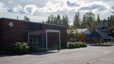 Ingång till en skolbyggnad i tegel. På väggen finns en klocka.