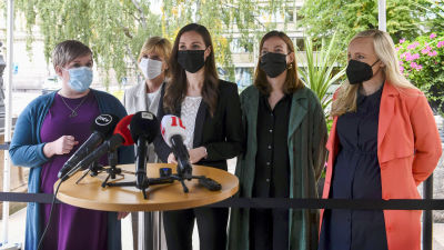 Annika Saarikko, Anna-Maja Henriksson, Sanna Marin, Li Andersson och Maria Ohisalo står framför ett talarpodium utanför Ständerhuset.