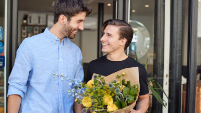 Två unga män ler mot varandra, den ena håller i en blombukett