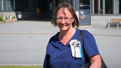 Kvinna i sjukhuskläder står framför en betongbyggnad.