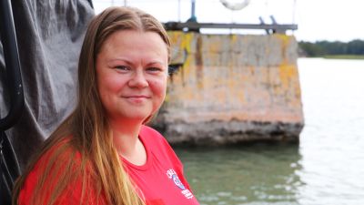 En kvinna med röd t-skjorta sitter utomhus med en stenbrygga i bakgrunden.