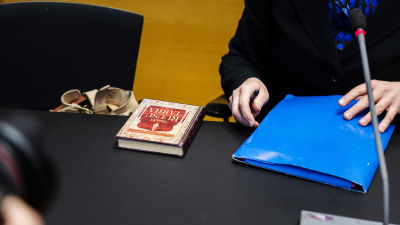 Boken Rosengården på ett bord bredvid en blå mapp och Tytti Yli-Viikaris händer.