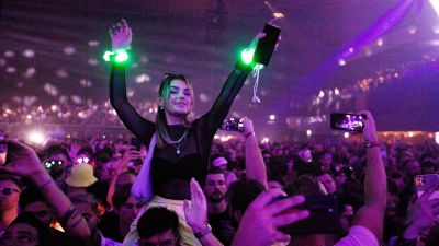 En kvinna sitter på en persons axlar på en konsert. Hon har händerna uppe i luften.