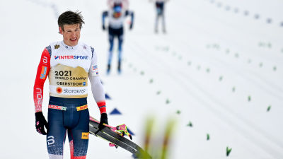 Johannes Høsflot Klæbo går med skidorna i vänsterhanden.