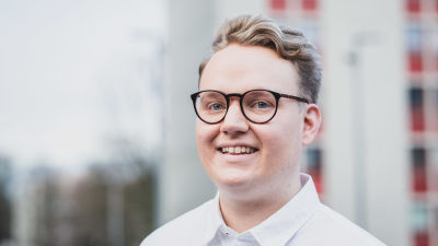 Ung man i glasögon och vit skjorta ler på bilden.