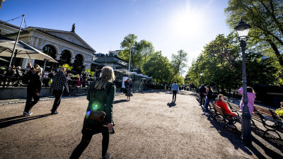 Människor går längs med sandvägen på Esplanadparken i Helsingfors. Solen skiner.