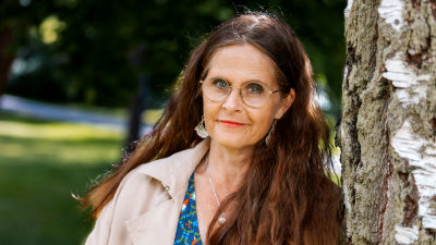 Toimittaja Liisa Vihmanen seisoo koivun edessä ja katsoo kameraan.