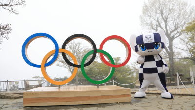 OS-maskoten står bredvid de olympiska ringarna.