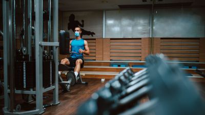 En man i munskydd tränar på gym.