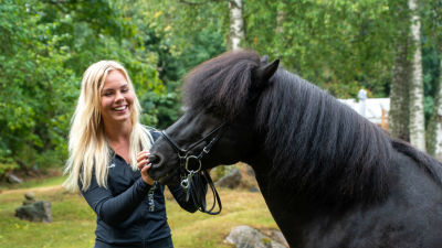 Arnella Nyman bredvid sin mörkbruna islandshäst Thór utomhus i en grön miljö.