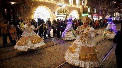 Kvinnor i vita o guldiga klänningar deltar i julparad.
