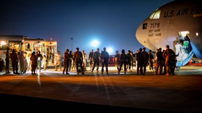 Upplyst flygplats där människor kliver ut ur ett flygplan på väg till väntande bussar. Evakuerade afghaner landar i Kuwait den 24 augusti.